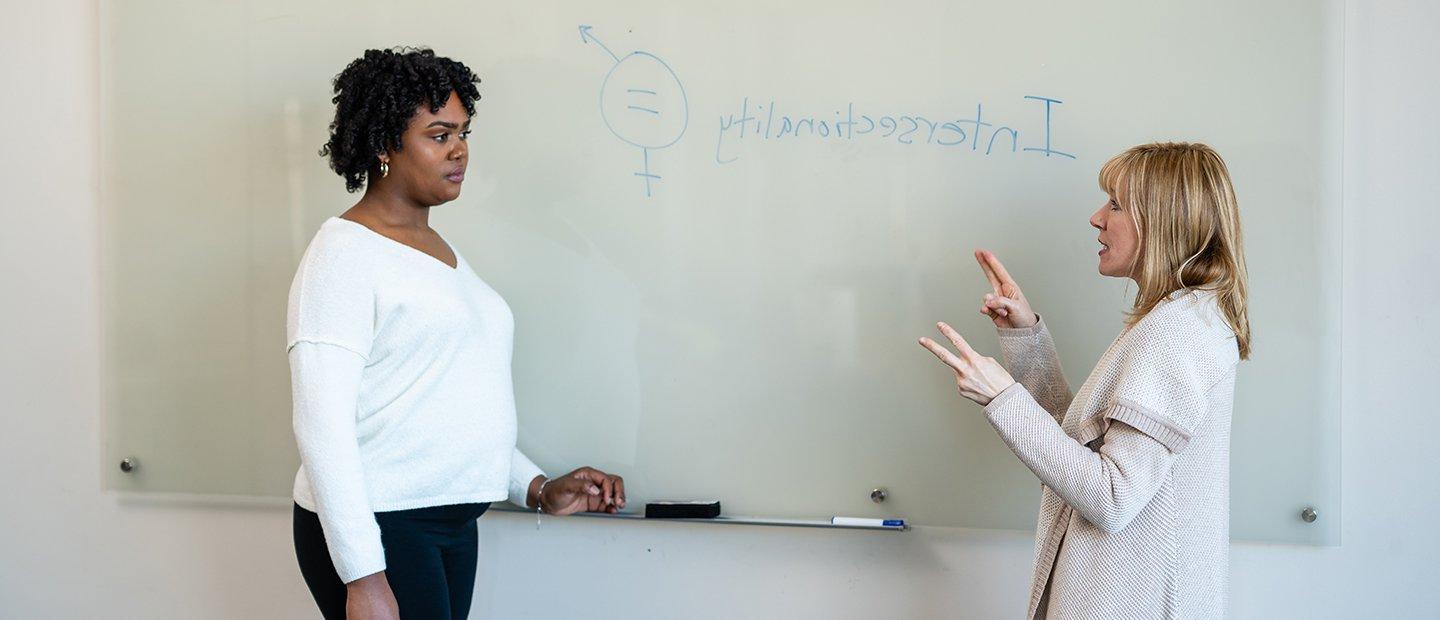 Two women standing in front of a white board